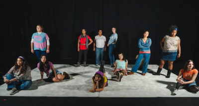 A group of women on a white carpet. Some are sitting on thefloor, a few are lying down, and others are standing